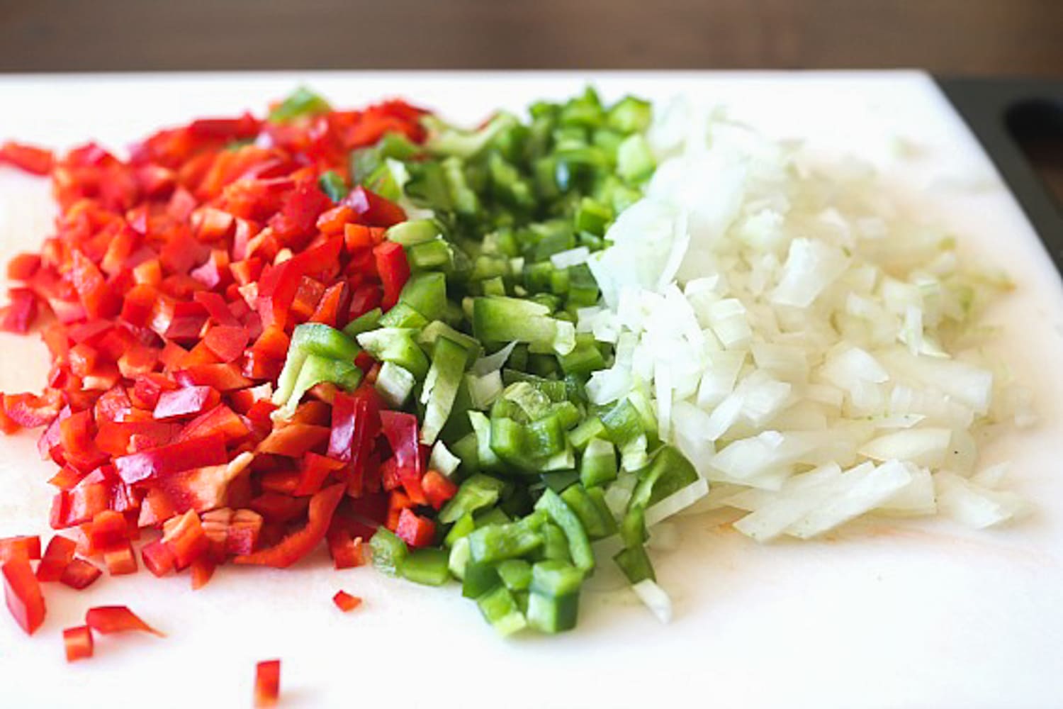 red bell peppers, green bell peppers, and onion diced on a white cutting board