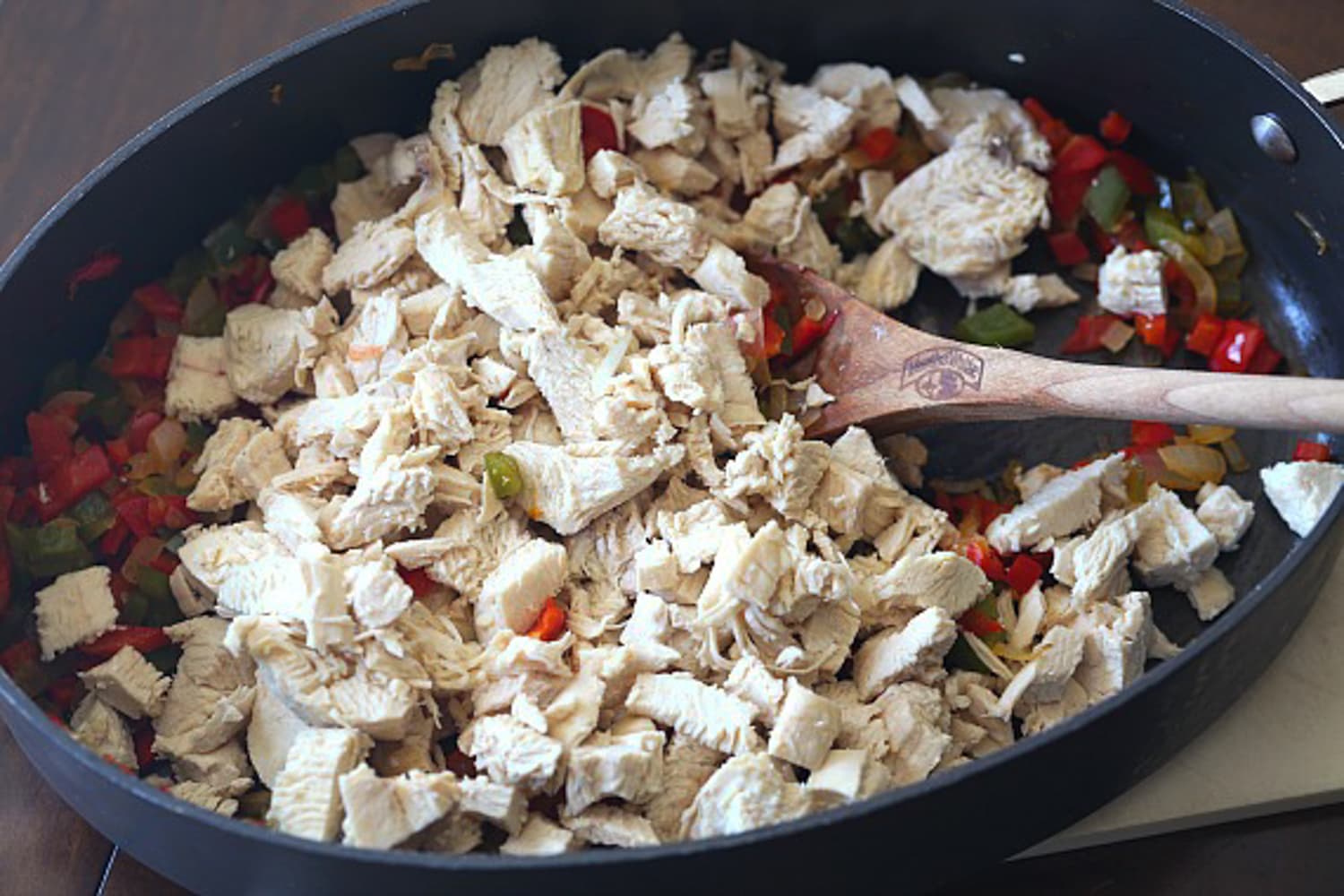 adding diced chicken breast to a deep nonstick skillet with a wooden spoon