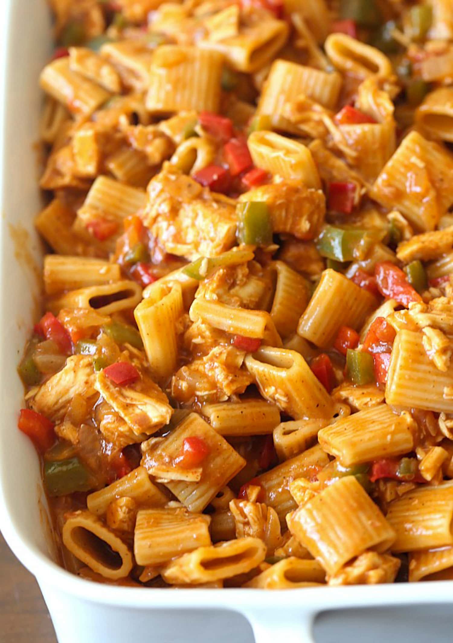 Chicken Enchilada Pasta added into a deep white casserole dish with bell peppers