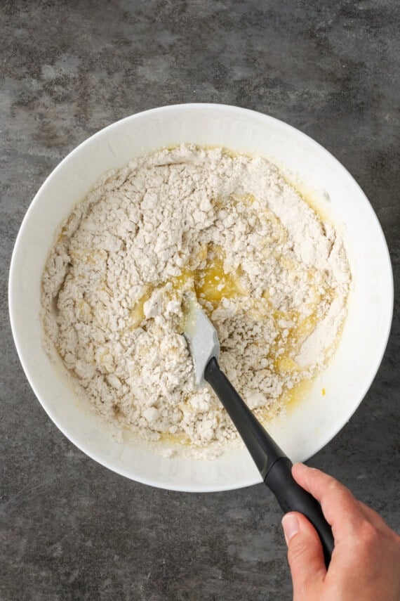 Ingredients for lemon pound cake batter stirred together in a white bowl with a spatula.