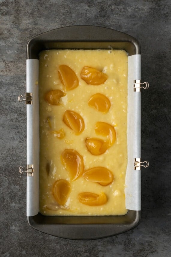 Overhead view of lemon curd dolloped into lemon pound cake batter in a lined loaf pan.