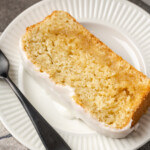 A slice of glazed lemon pound cake on a white plate next to a fork.