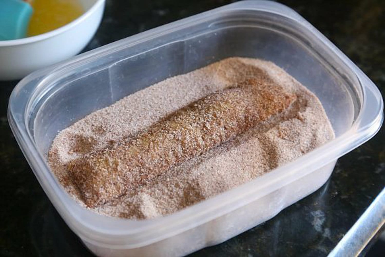 Dipping butter-coated churro into cinnamon sugar