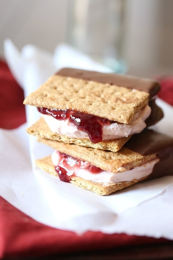 Two Chocolate Dipped Strawberry Cheesecake Sandwiches stacked on a white cloth.