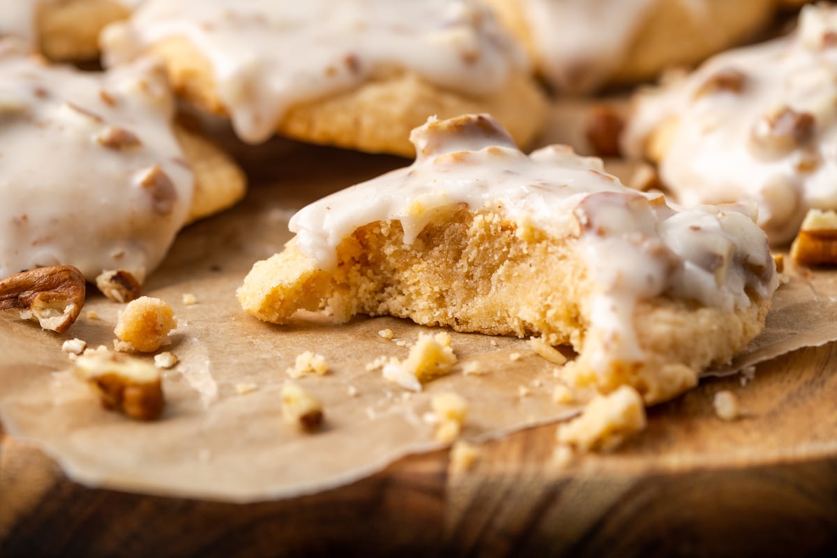 A glazed butter pecan cookie on a wooden platter with a bite missing, and more cookies in the background.