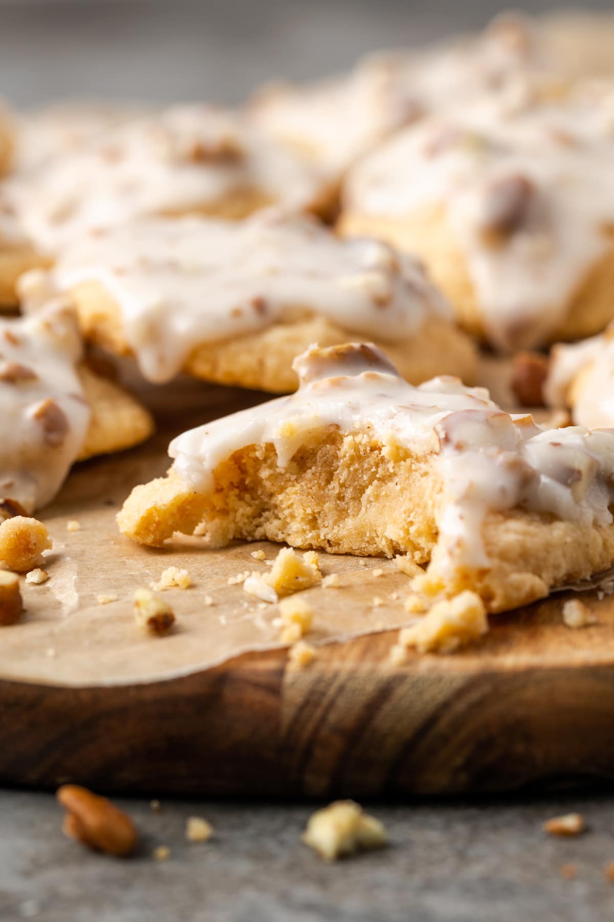 A glazed butter pecan cookie on a wooden platter with a bite missing, and more cookies in the background.