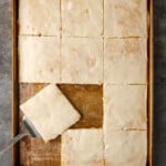 Top view of a frosted buttermilk sheet cake with a slice being served from the corner.