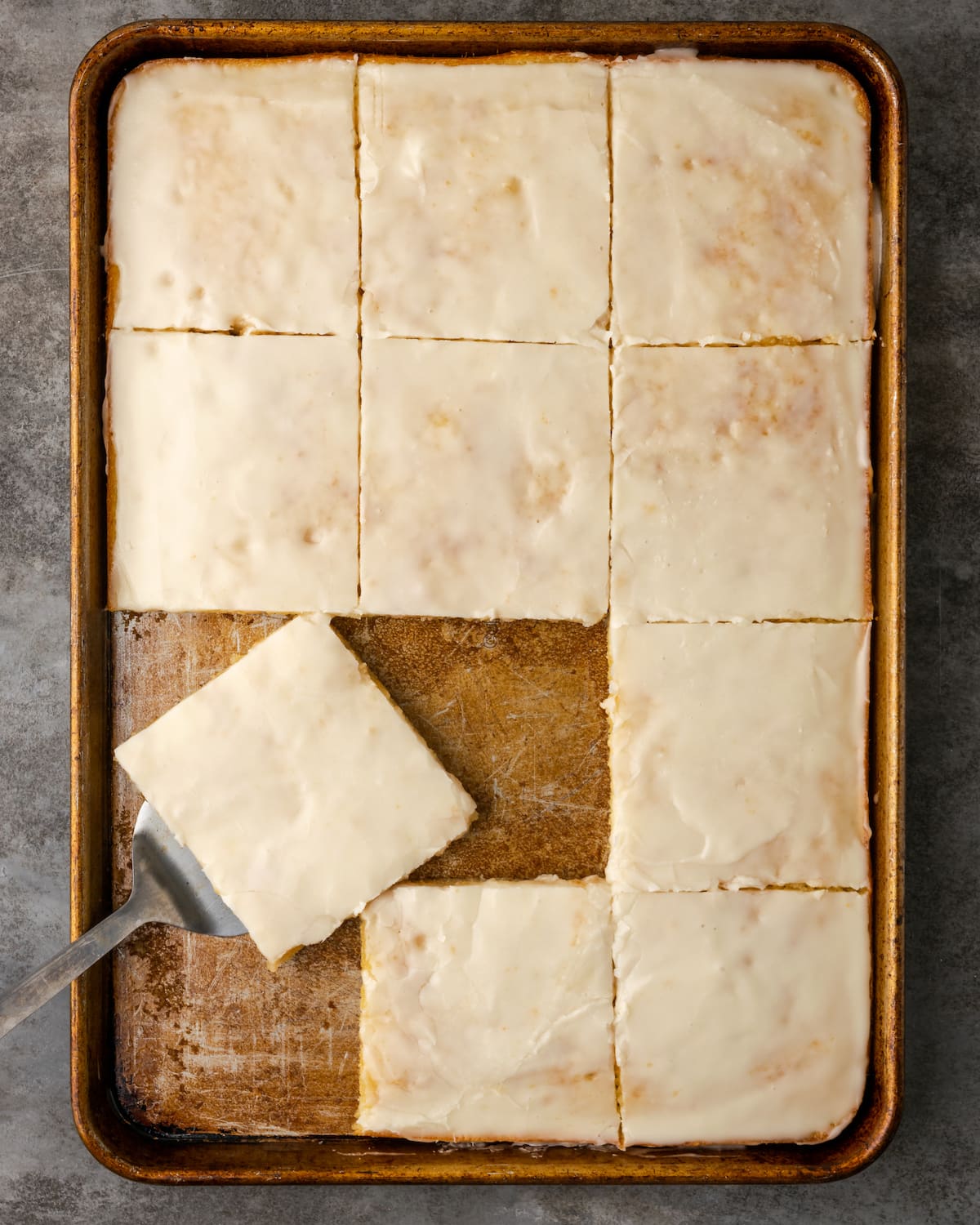 Top view of a frosted buttermilk sheet cake with a slice being served from the corner.