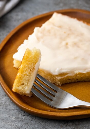 Close up of a forkful of buttermilk sheet cake on a plate next to a cake slice.