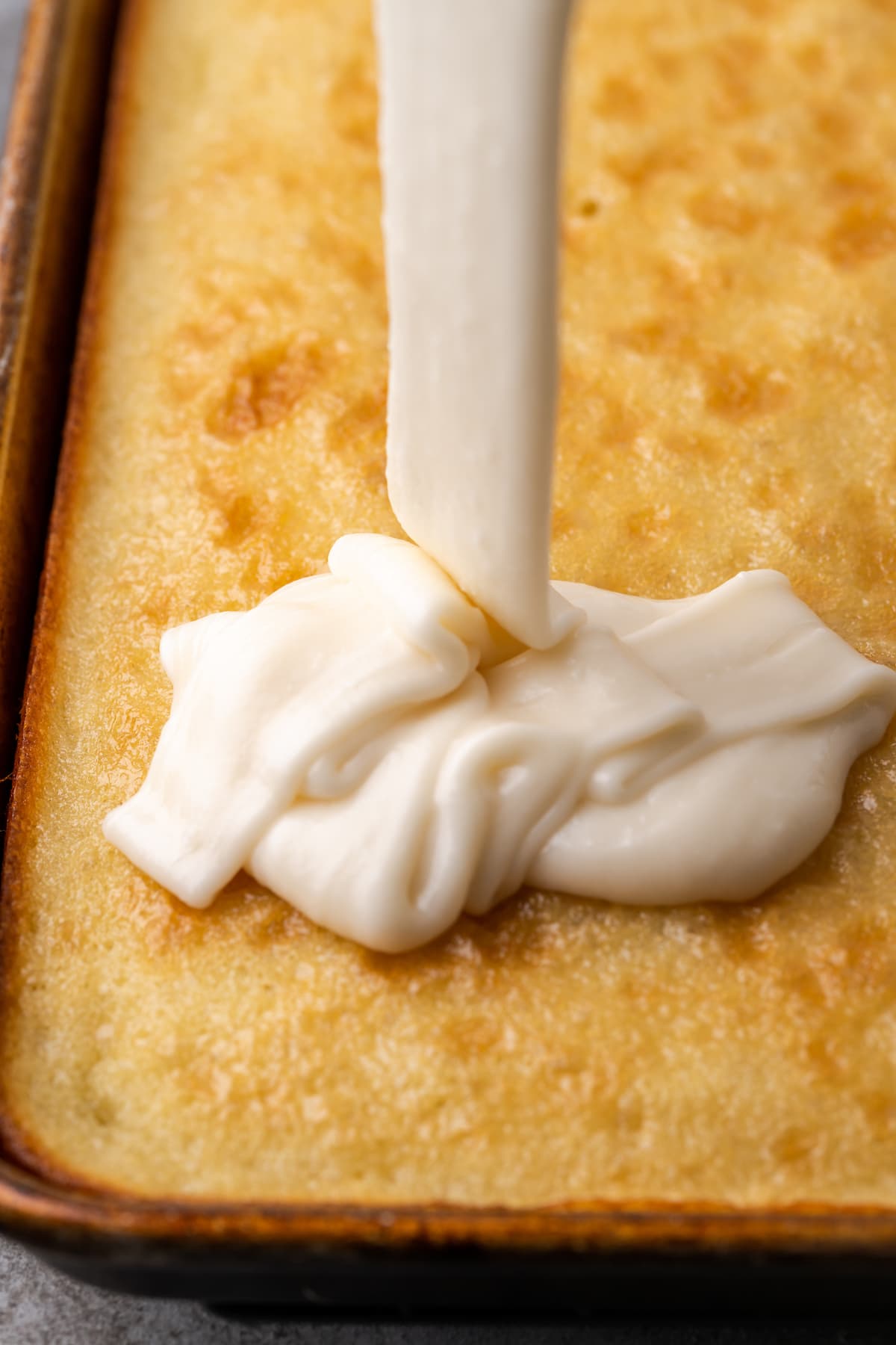 Vanilla frosting is drizzled into a baked buttermilk sheet cake.