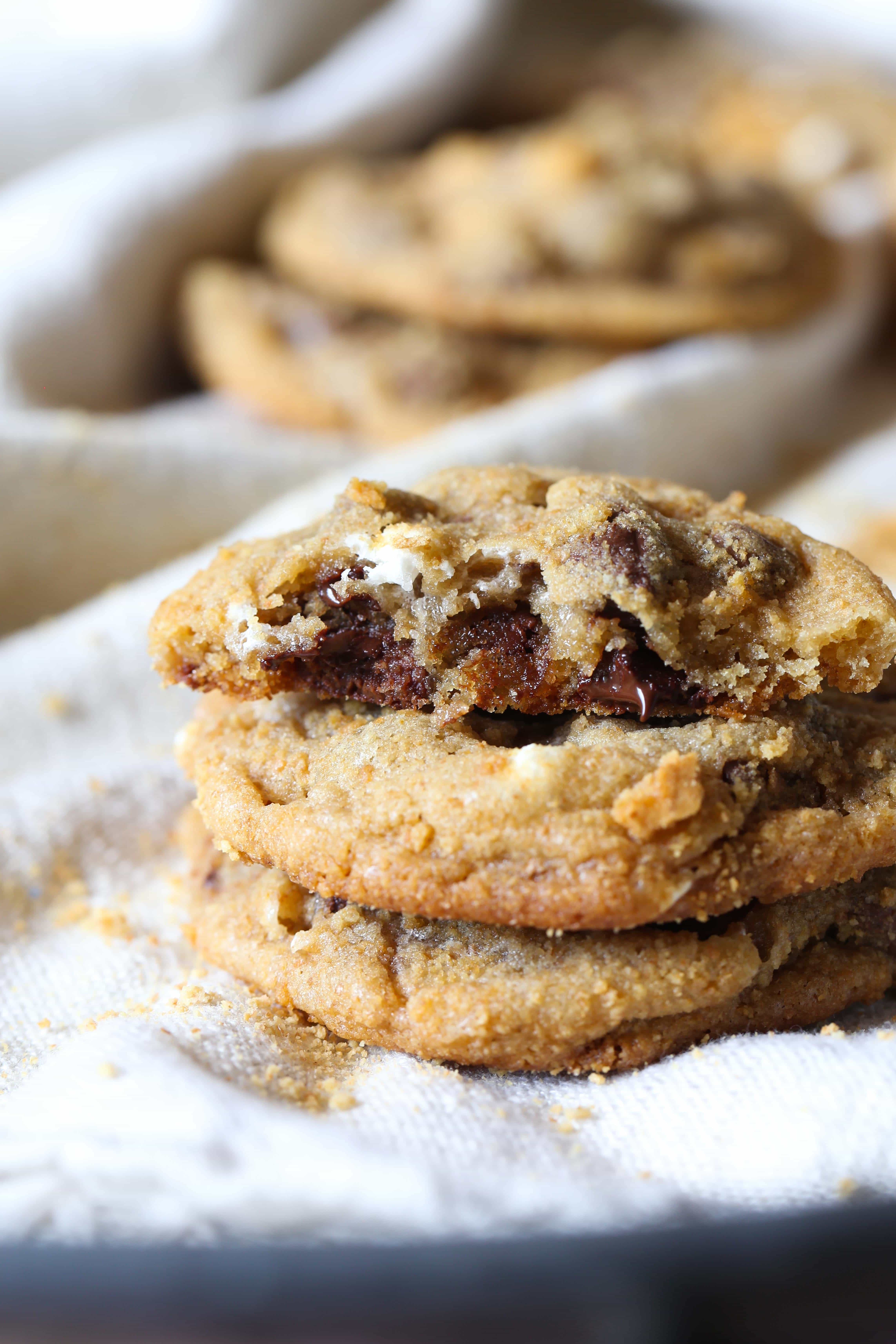 These easy s’more chocolate chip cookies are filled with melty chocolate and mini marshmallows and covered in graham cracker crumb "dirt"! S'more chocolate chip cookies stacked with a bite missing from the top cookie.
