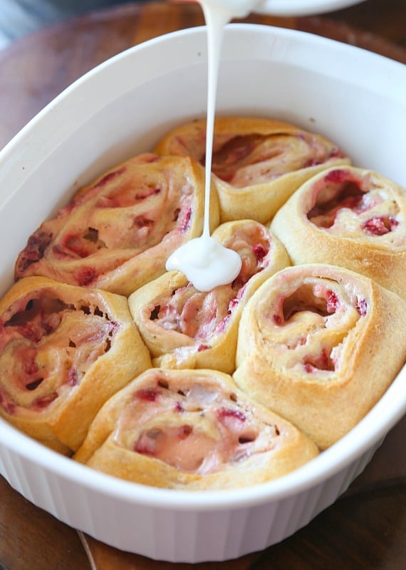 Quick and easy strawberry cinnamon rolls are soft, gooey, and loaded with fresh strawberries rolled inside refrigerated crescent roll dough. Drizzling icing over freshly baked strawberry cinnamon rolls in a baking dish.