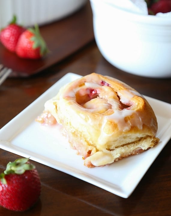 Quick and easy strawberry cinnamon rolls are soft, gooey, and loaded with fresh strawberries rolled inside refrigerated crescent roll dough. A sweet strawberry roll on a plate.