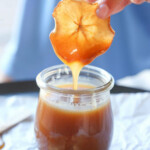 A dried apple slice being dipped in a jar of caramel sauce