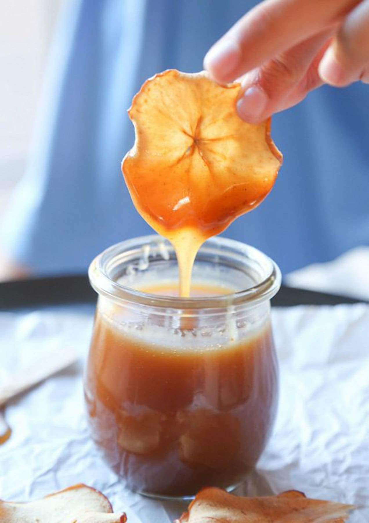 A dried apple slice being dipped in a jar of caramel sauce