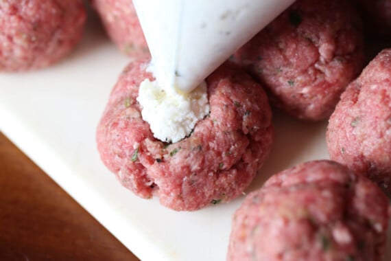 Ricotta cheese being piped into the center of a meatball.