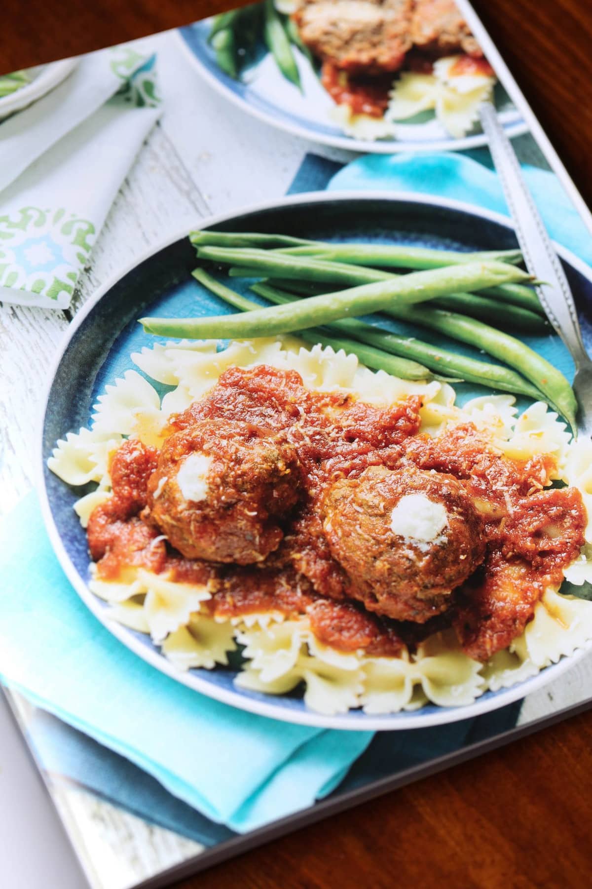 Slow cooker ricotta stuffed meatballs served over pasta on a plate, with a bite missing from one meatball.
