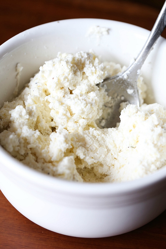 Ricotta cheese mixture in a white mixing bowl with a spoon.