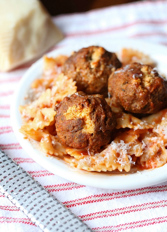 Slow cooker ricotta stuffed meatballs served over pasta on a plate set on top of a striped cloth.