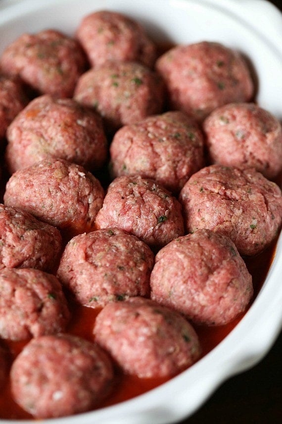 Uncooked ricotta stuffed meatballs inside the bowl of a slow cooker.