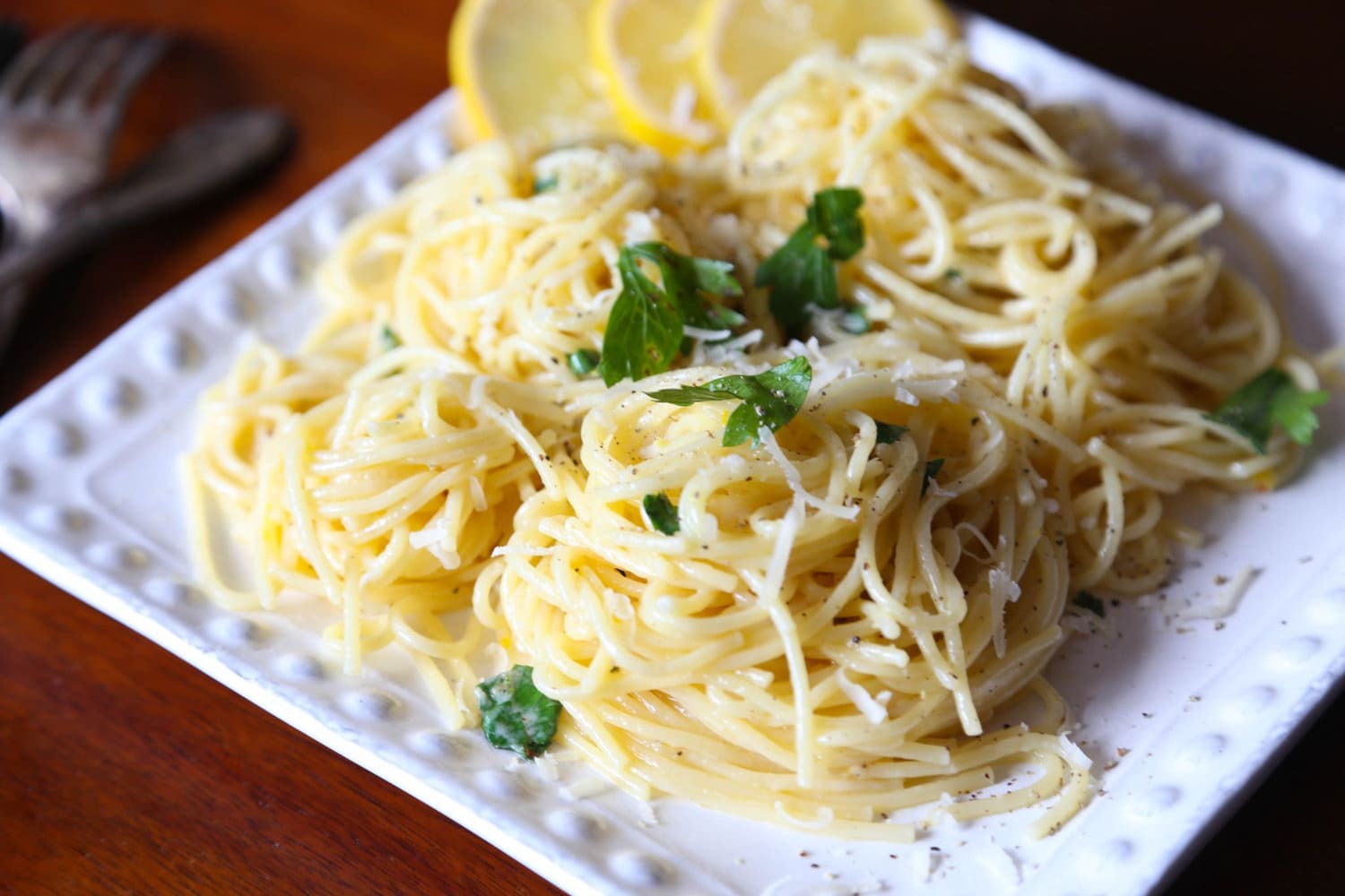 Lemon spaghetti served on a plate, garnished with fresh herbs and lemon slices.