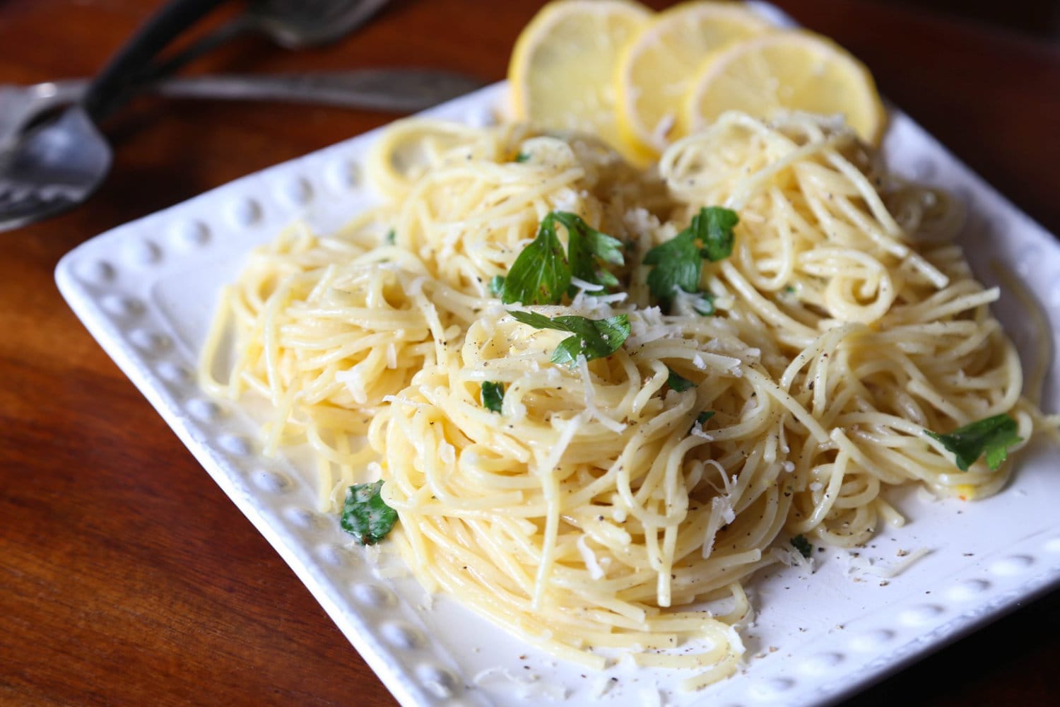 Lemon spaghetti served on a plate, garnished with fresh herbs and lemon slices.