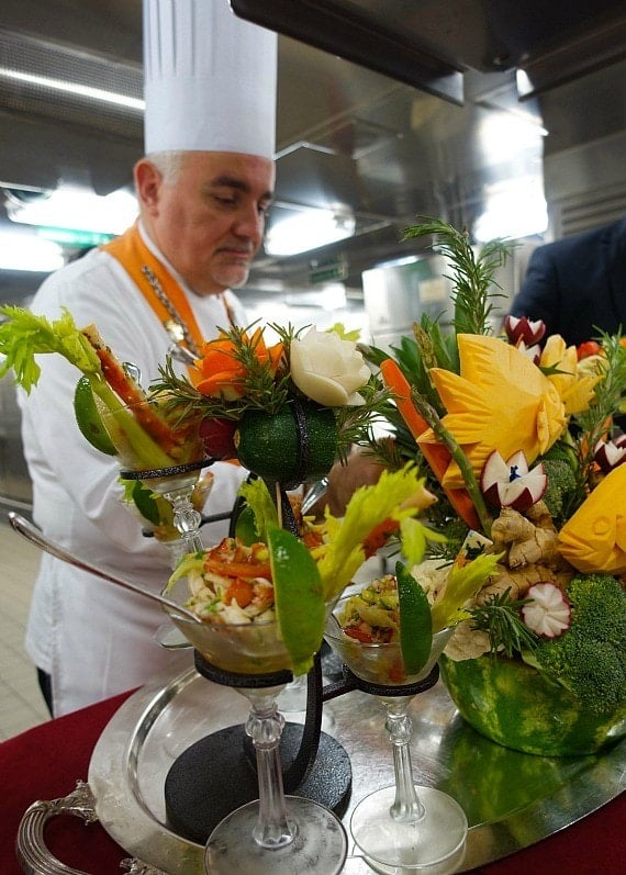 A chef with an orange sash making food disguised as floral arrangements