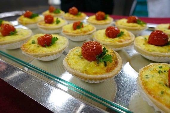 Fourtteen servings of crab ceviche lined up on a glass display shelf