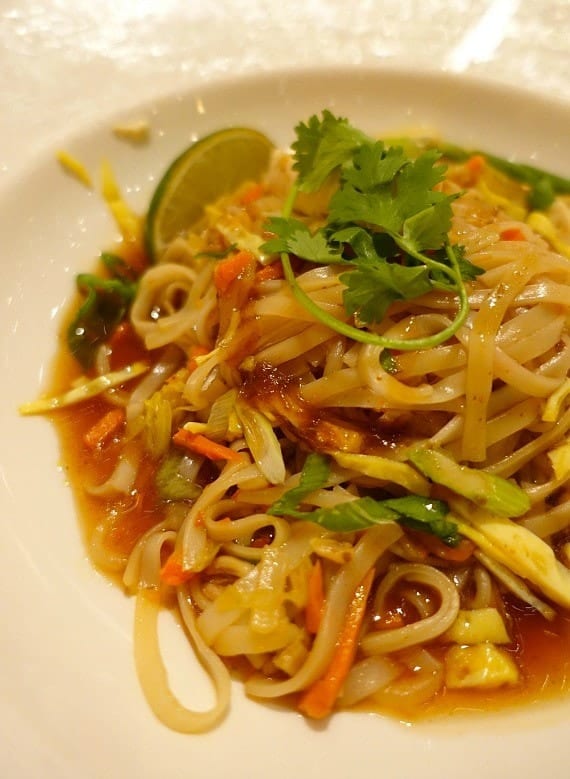 A plate of Pad Thai garnished with fresh parsley and a lime slice