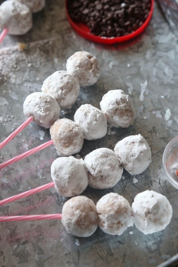 Powdered donut holes threaded onto four cake pop sticks, laying on their side on a countertop.