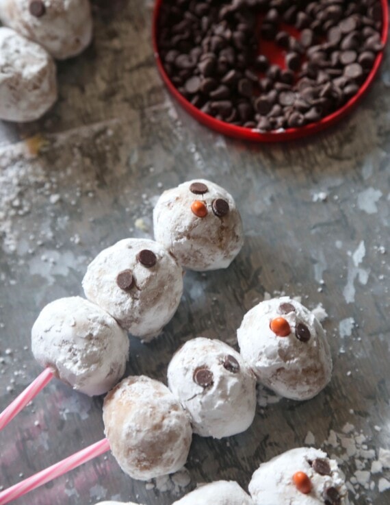 Three snowman cake pops on sticks with chocolate chips as the eyes and buttons.