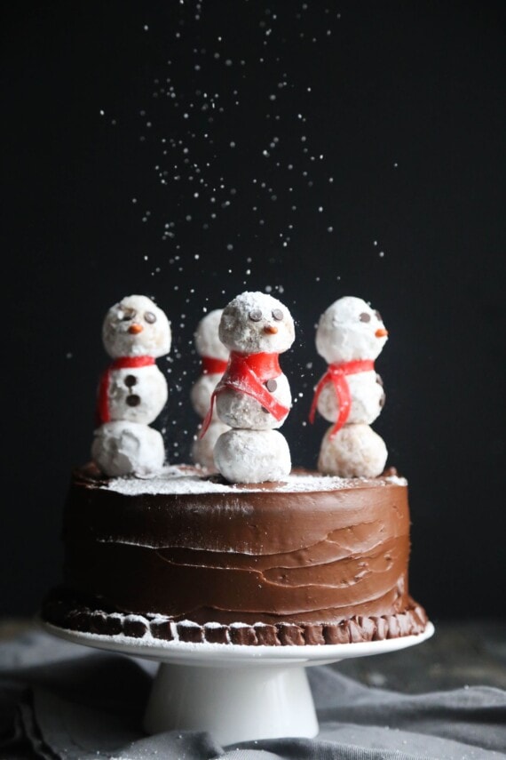 Side view of a snowman cake being dusted with powdered sugar from above.