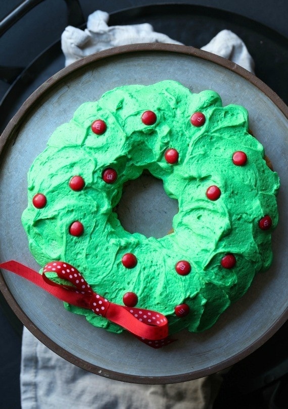 Overhead view of a green wreath cake with red candies and a bow