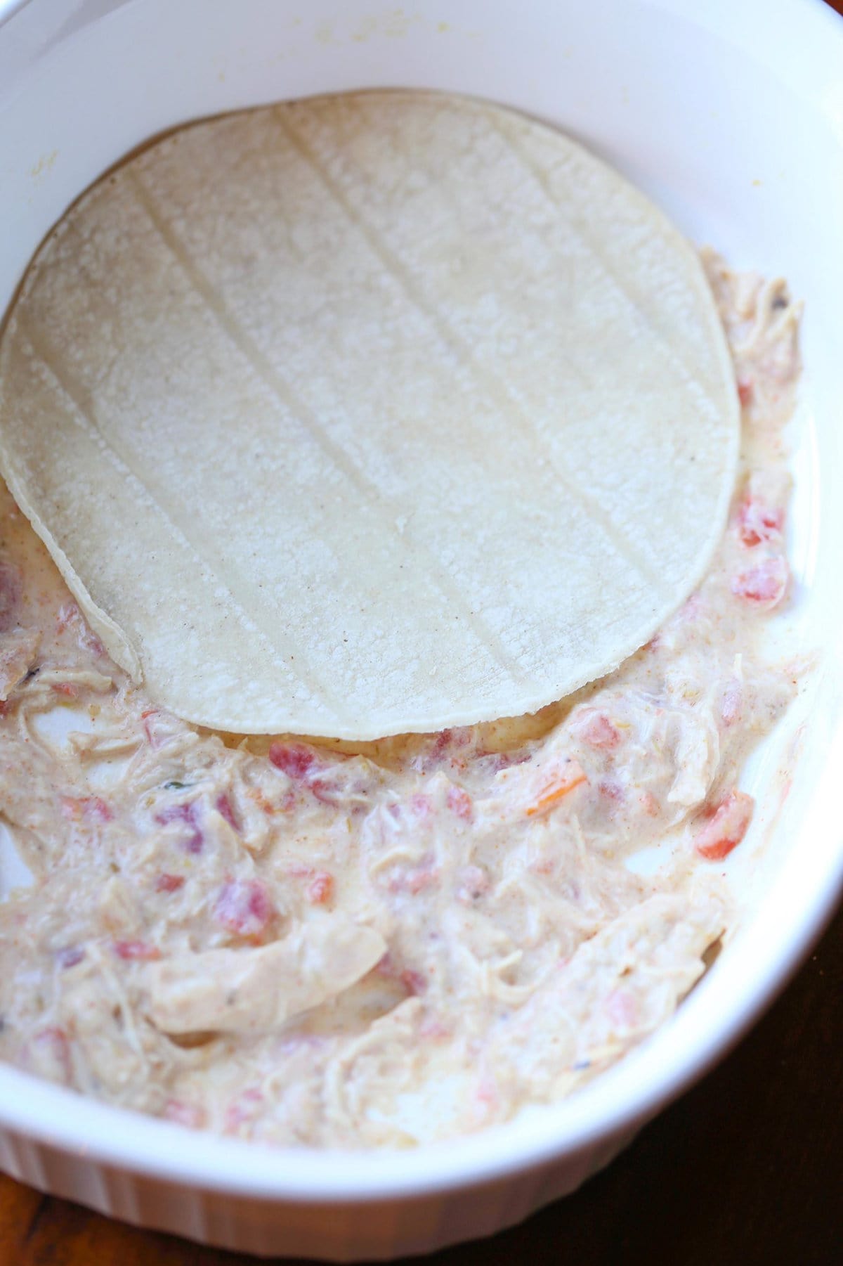 A single flour tortilla placed over salsa verde chicken mixture in a casserole dish.