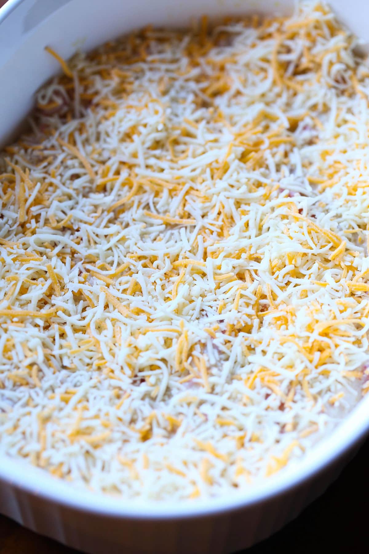 Shredded cheese layered over tortillas while assembling a salsa verde chicken casserole in a baking dish.