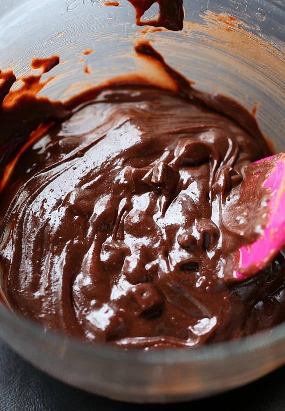 A pink spoon is used to stir brownie batter in a mixing bowl.