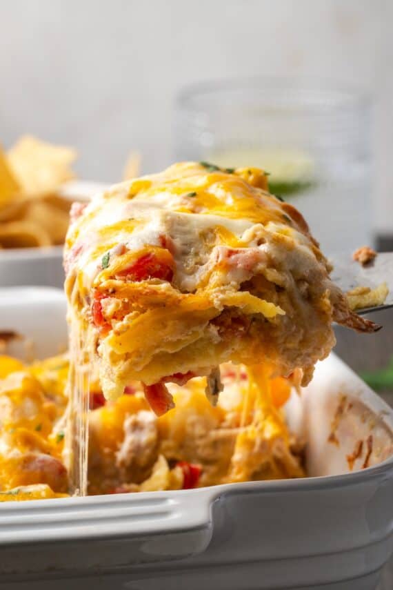 A serving of salsa verde chicken casserole being lifted from a baking dish with a spatula.