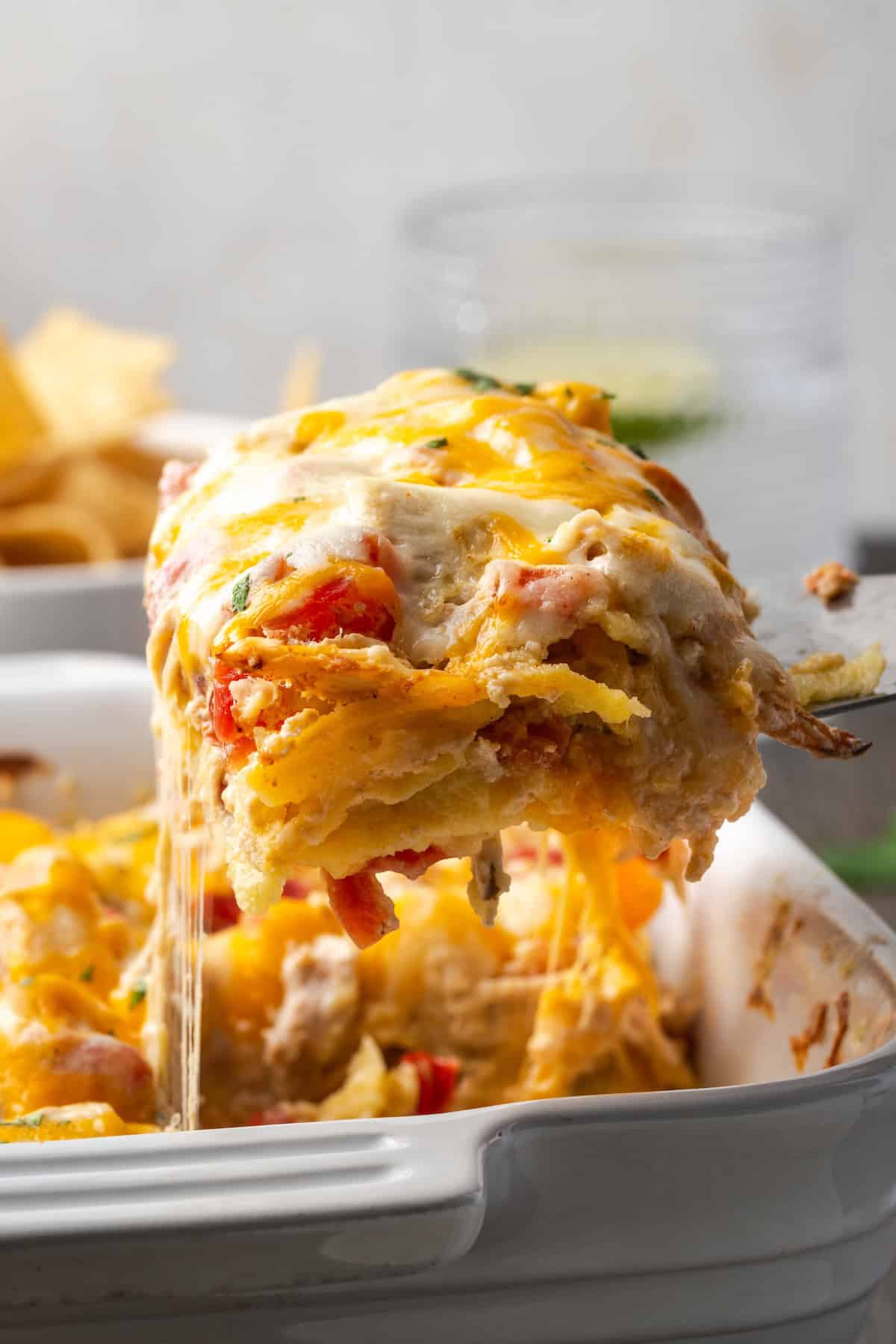 A serving of salsa verde chicken casserole being lifted from a baking dish with a spatula.