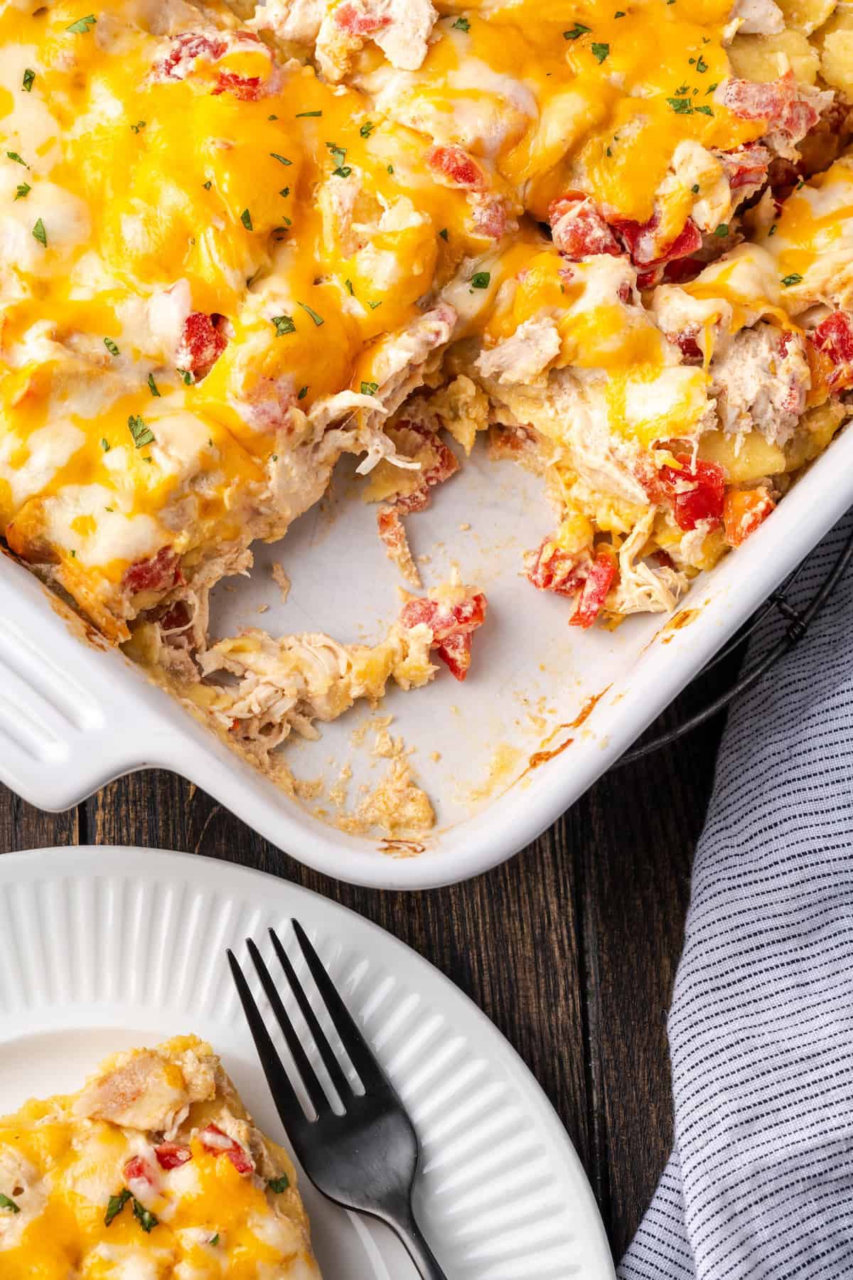 Overhead view of salsa verde chicken casserole in a baking dish, next to a slice served on a white plate next to a fork.