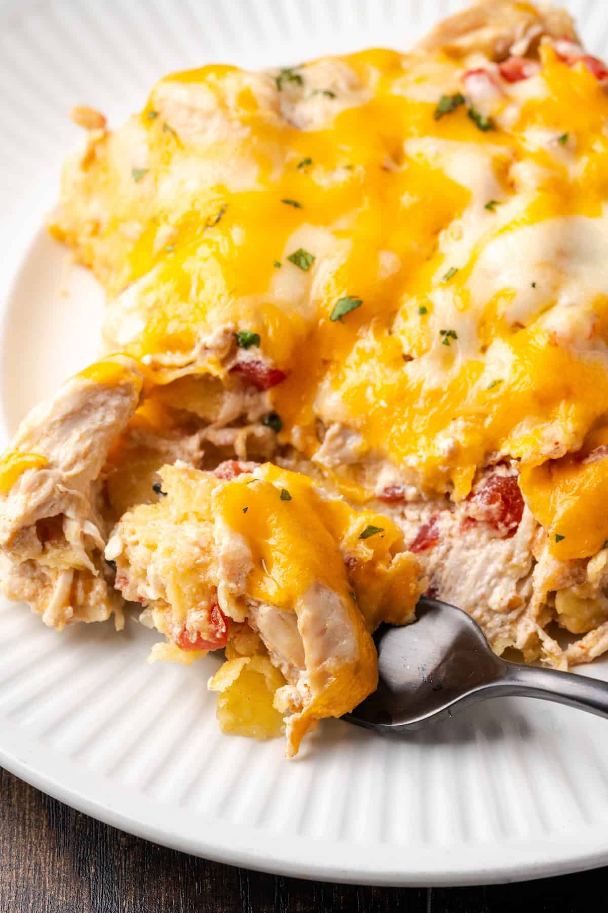 Close up of a forkful of salsa verde chicken casserole next to a slice on a plate.