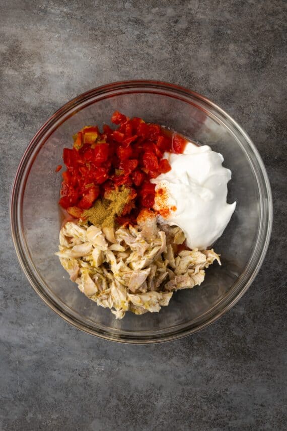 Salsa verde chicken, Rotel tomatoes, and sour cream combined in a bowl.