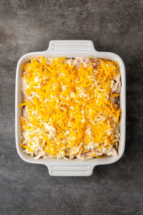 Assembled salsa verde chicken casserole topped with shredded cheese in a baking dish.