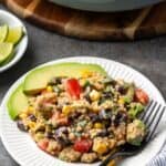 A serving of Southwestern quinoa salad next to avocado slices on a white plate with a fork.