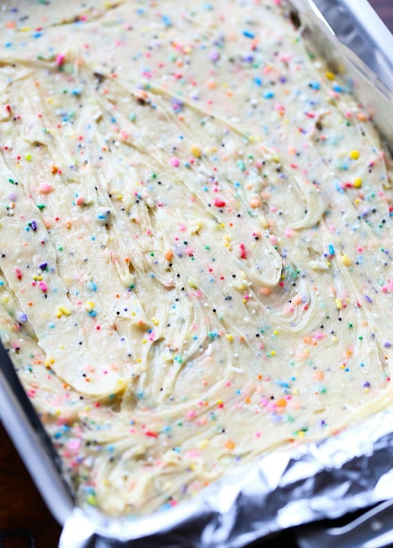 Unicorn bars are a fun, easy dessert! Buttery, soft-baked funfetti cookie bars loaded with rainbow sprinkles and frosted with homemade icing. Unicorn sugar cookie dough spread in a baking pan.