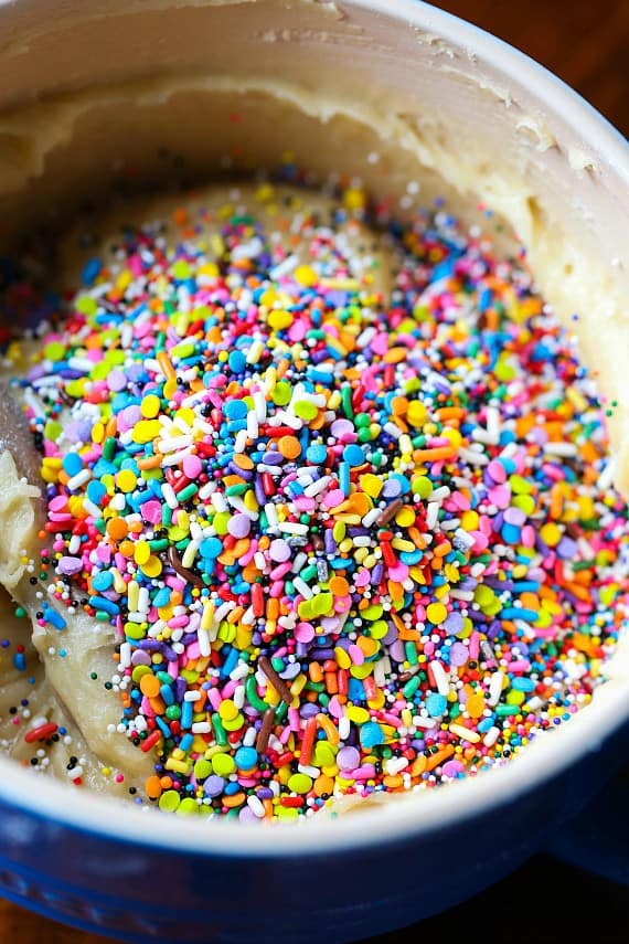 Unicorn bars are a fun, easy dessert! Buttery, soft-baked funfetti cookie bars loaded with rainbow sprinkles and frosted with homemade icing. Rainbow sprinkles added to sugar cookie dough in a bowl.