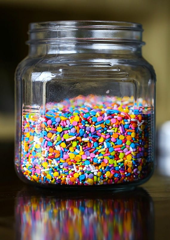 Unicorn bars are a fun, easy dessert! Buttery, soft-baked funfetti cookie bars loaded with rainbow sprinkles and frosted with homemade icing. A jar of rainbow sprinkles.