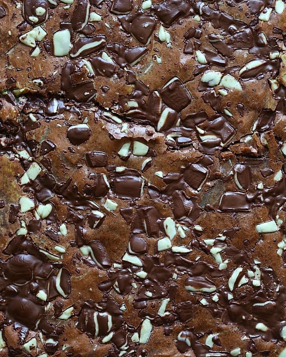 Close up of baked brownies topped with mint chocolate candy bars chopped into small pieces.