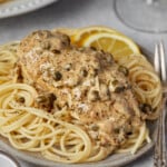 Chicken piccata served over pasta on a plate.