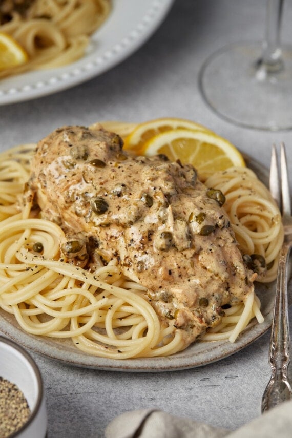 Chicken piccata served over pasta on a plate.