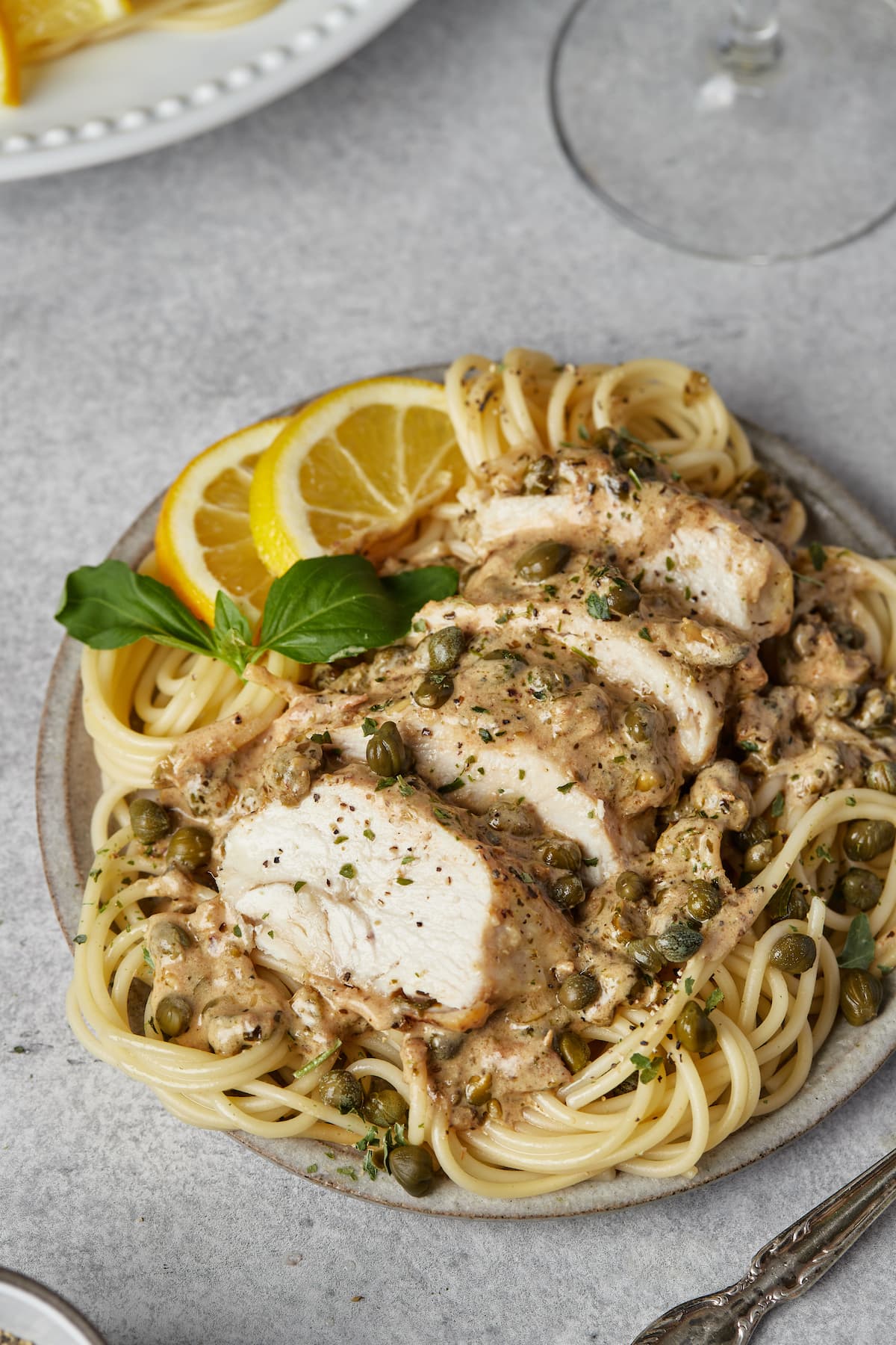 Sliced chicken piccata served over spaghetti and garnished with lemon slices.